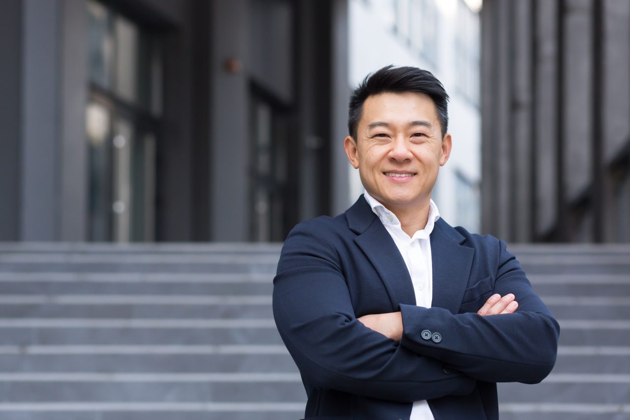 portrait of asian cheerful and successful businessman near office in business