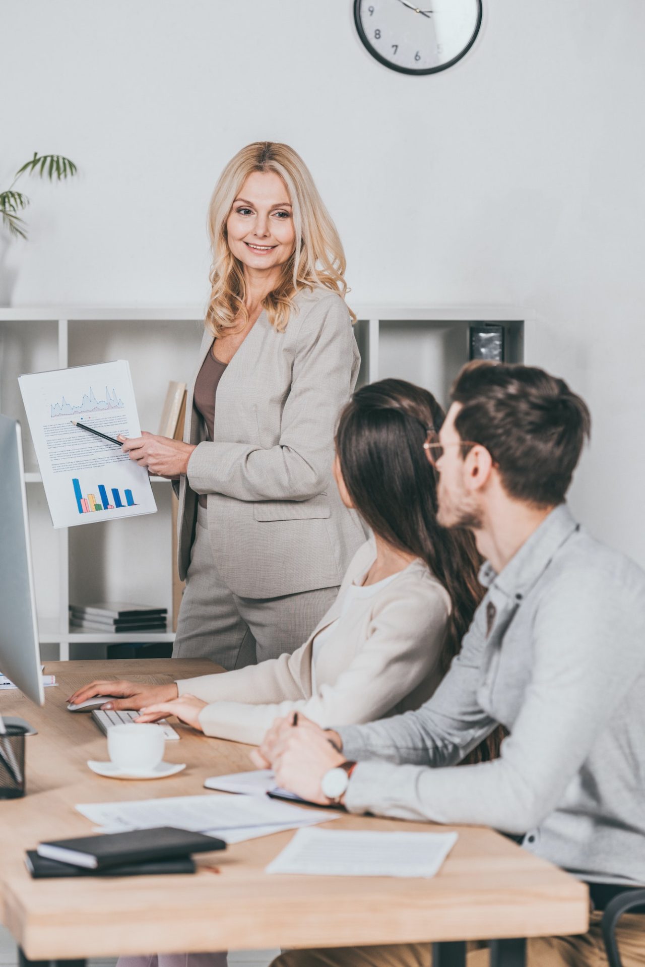 smiling mature businesswoman showing charts and graphs to young colleagues in office